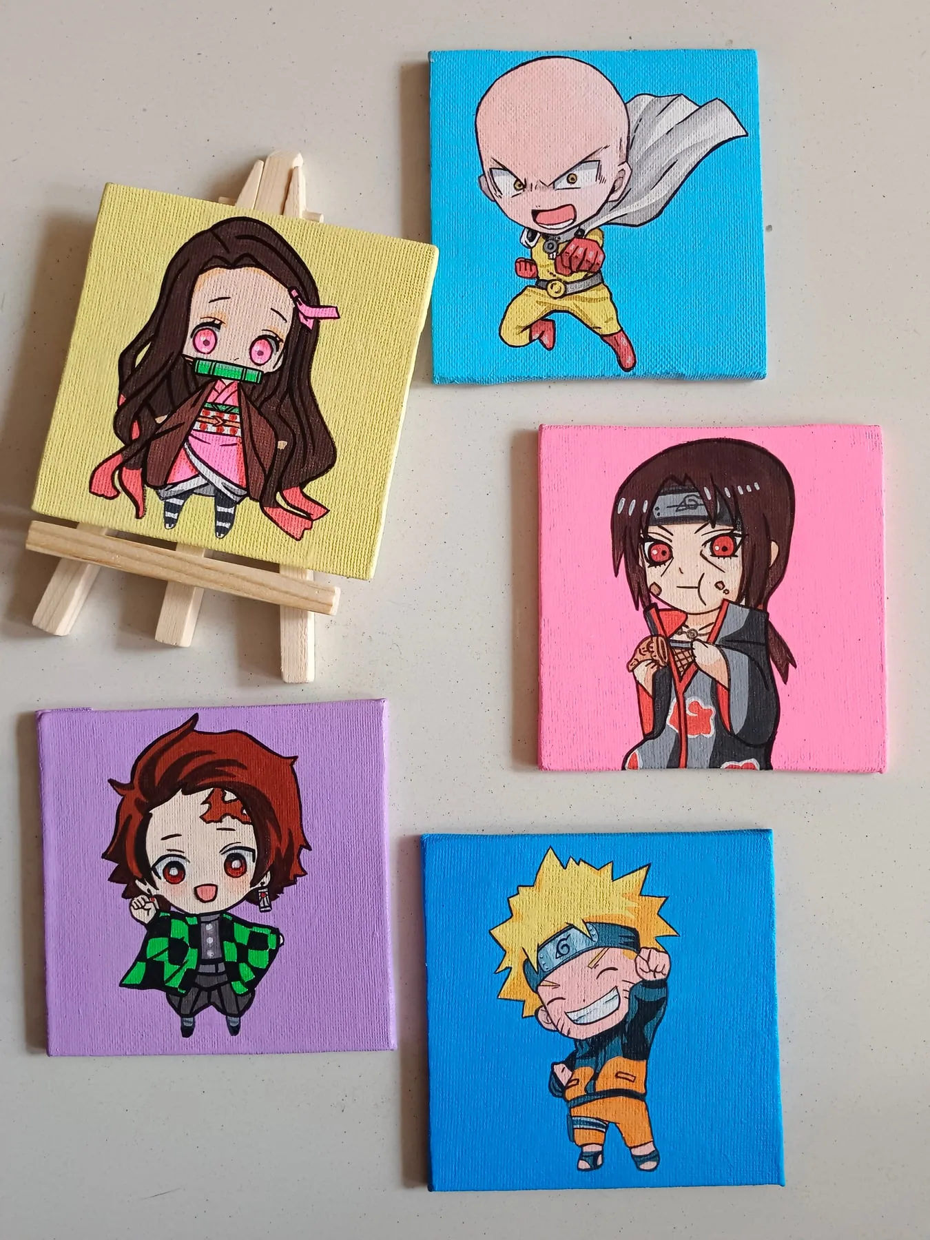 Display of small hand-painted acrylic mini canvases featuring Nezuko Kamado, Saitama, Tanjiro Kamado, Naruto Uzumaki and another character.