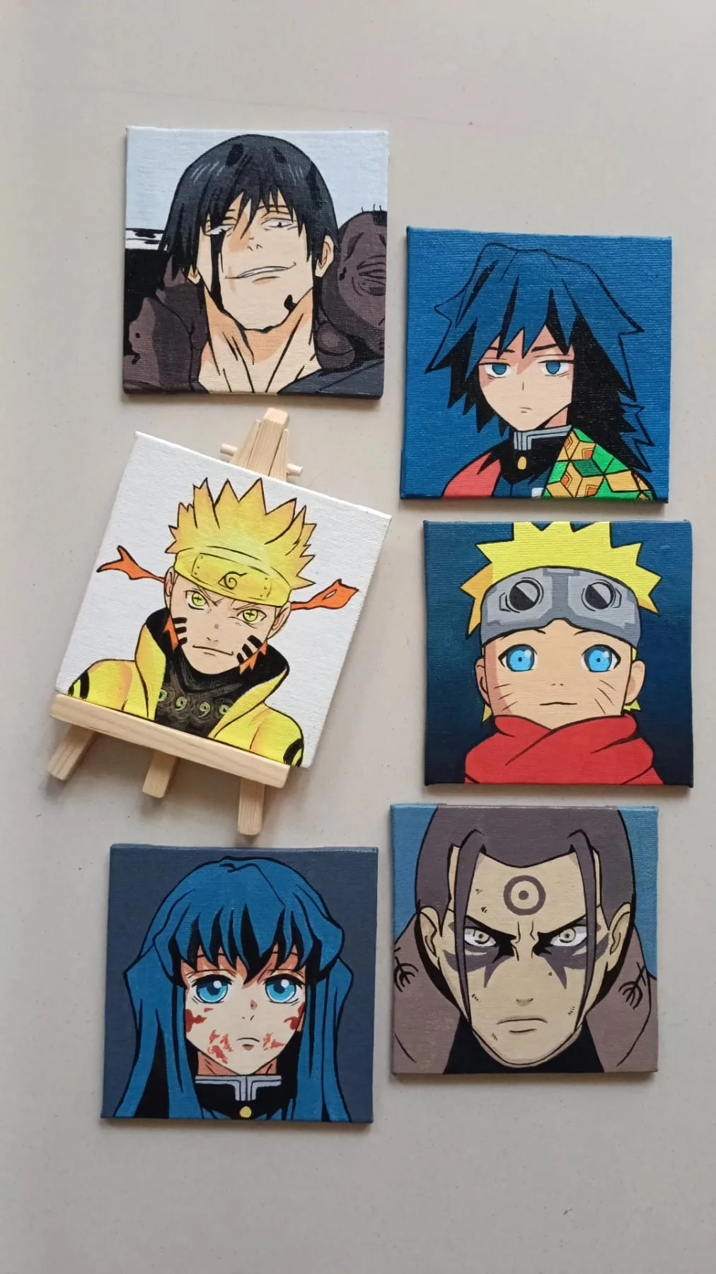 Shelf display of hand-painted acrylic Naruto and Demon Slayer mini canvases featuring Itachi Uchiha, Naruto Uzumaki and other character portraits.