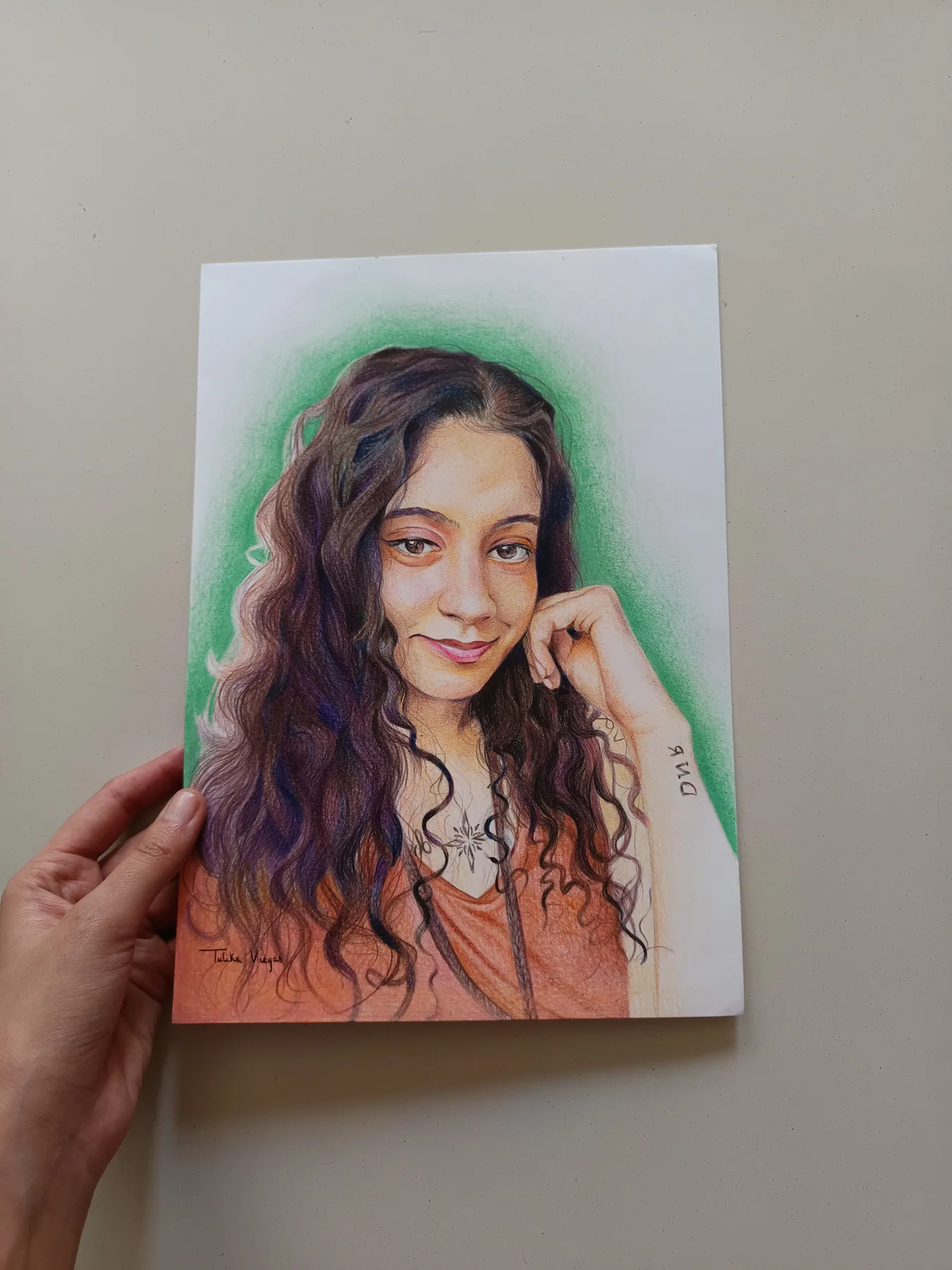 Colour-pencil portrait of a young woman with curly hair and a soft green background, held in hand.