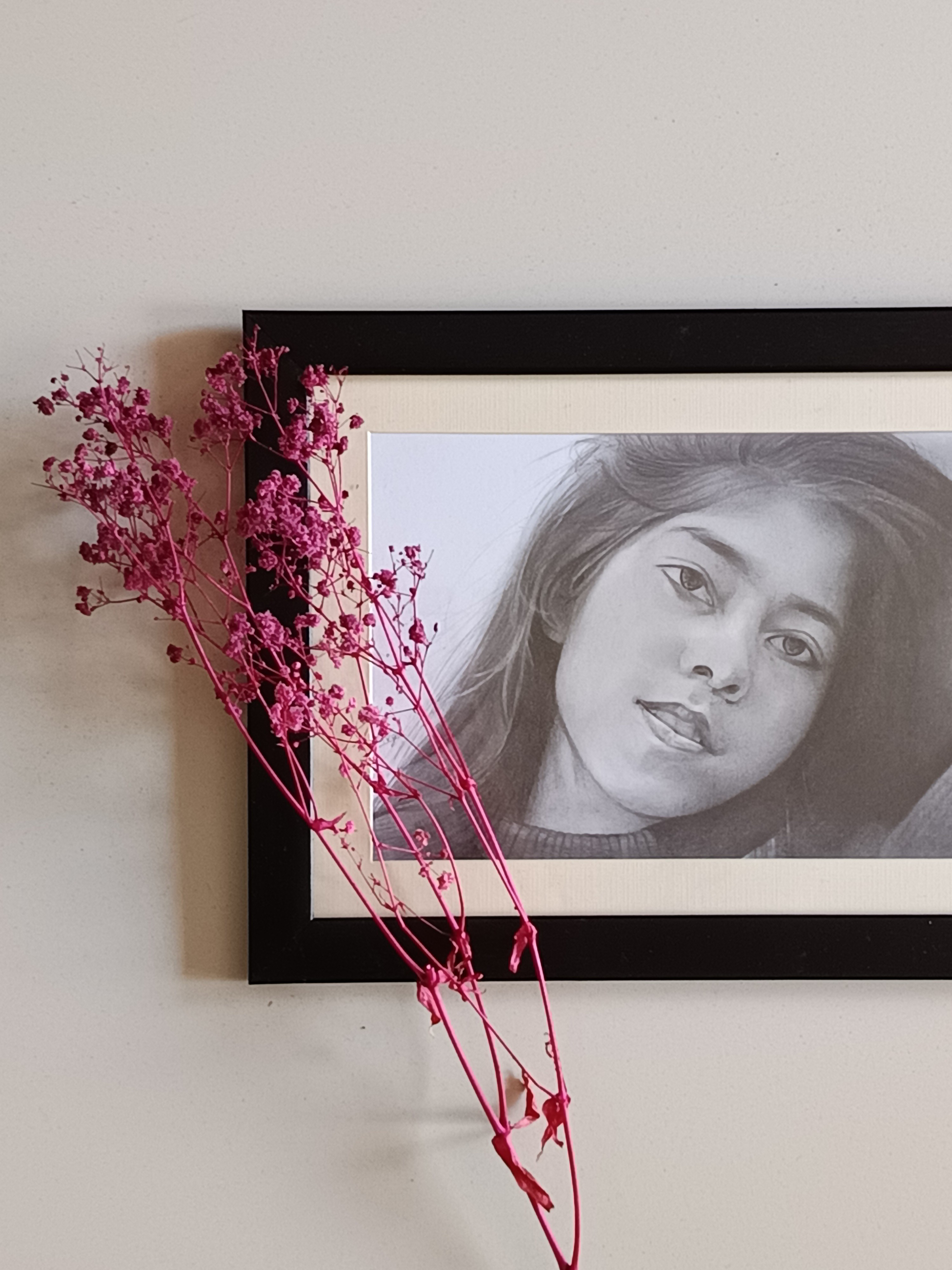 Framed graphite-pencil portrait of a young woman, displayed with pink dried flowers.