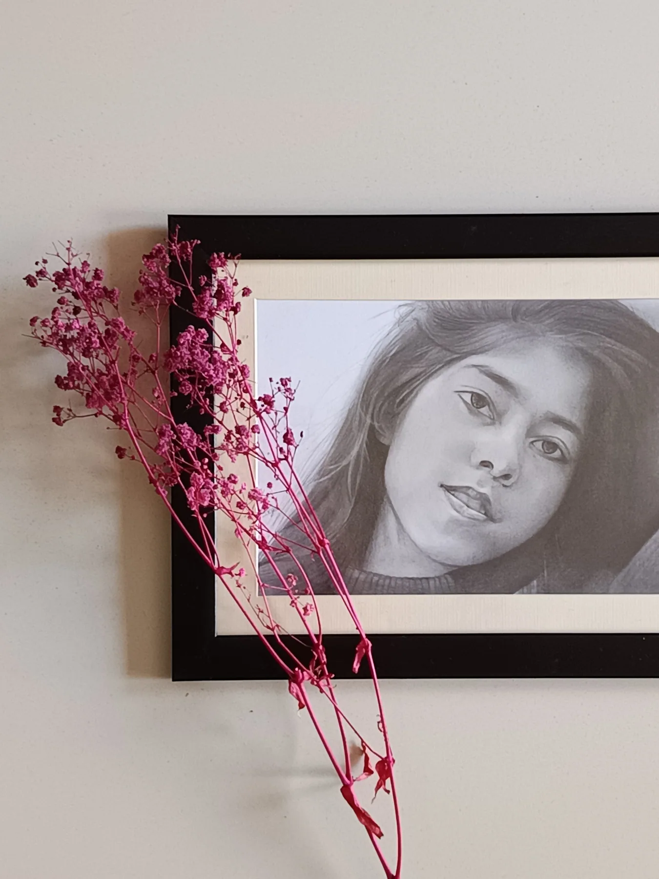 Framed graphite-pencil portrait of a young woman, displayed with pink dried flowers.