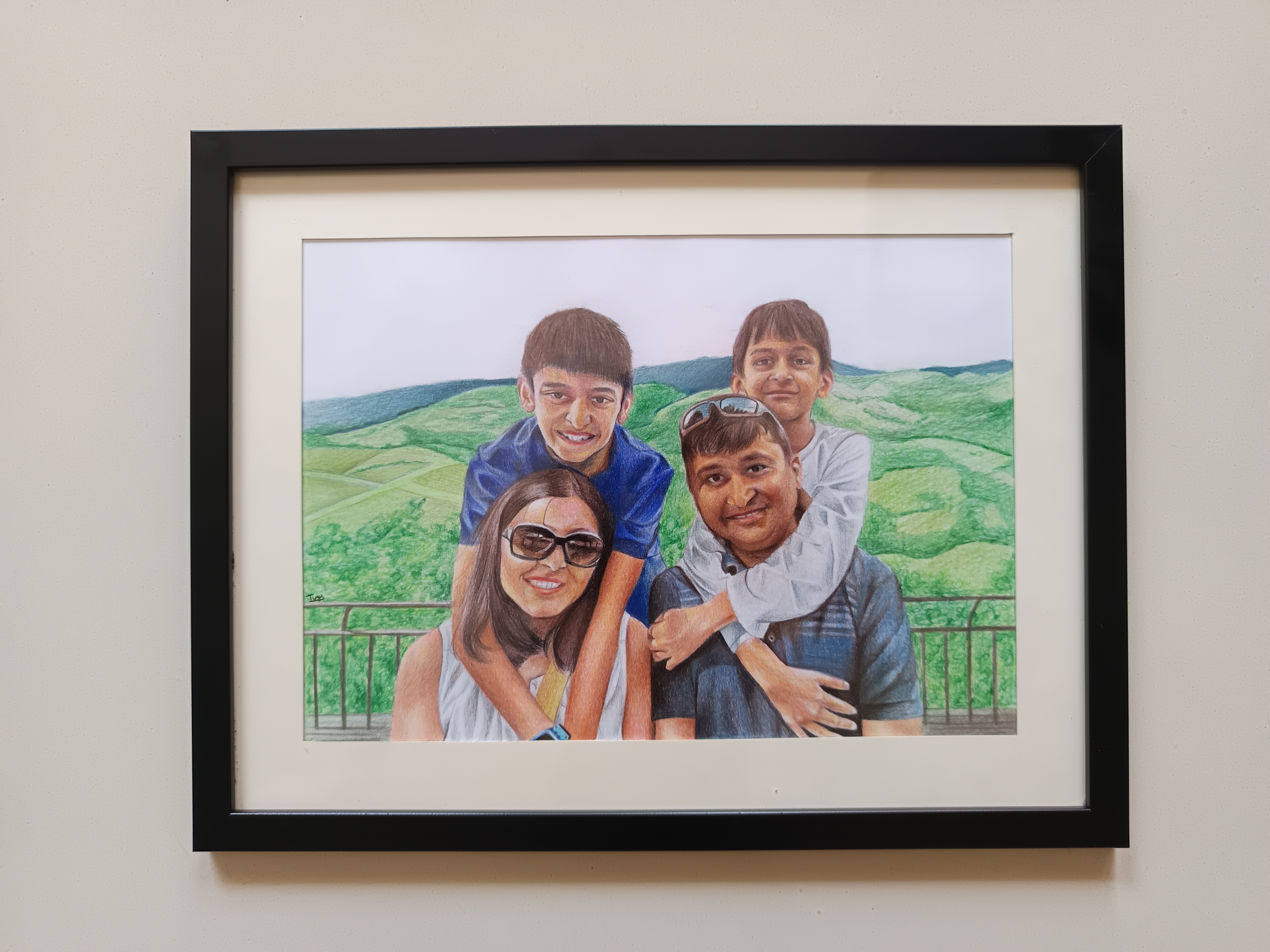 Framed colour-pencil family portrait with four people against a green landscape background.