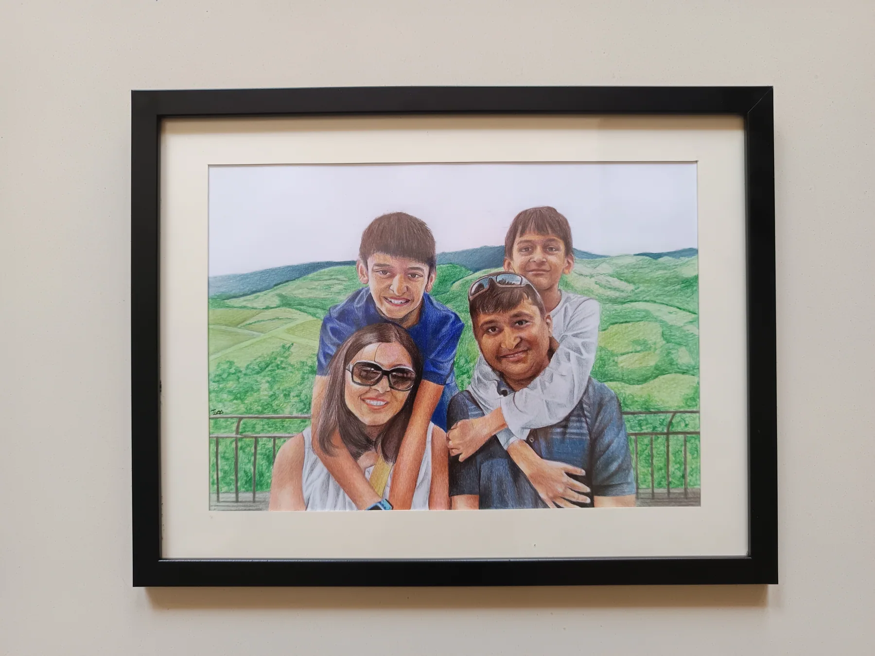 Framed colour-pencil family portrait with four people against a green landscape background.