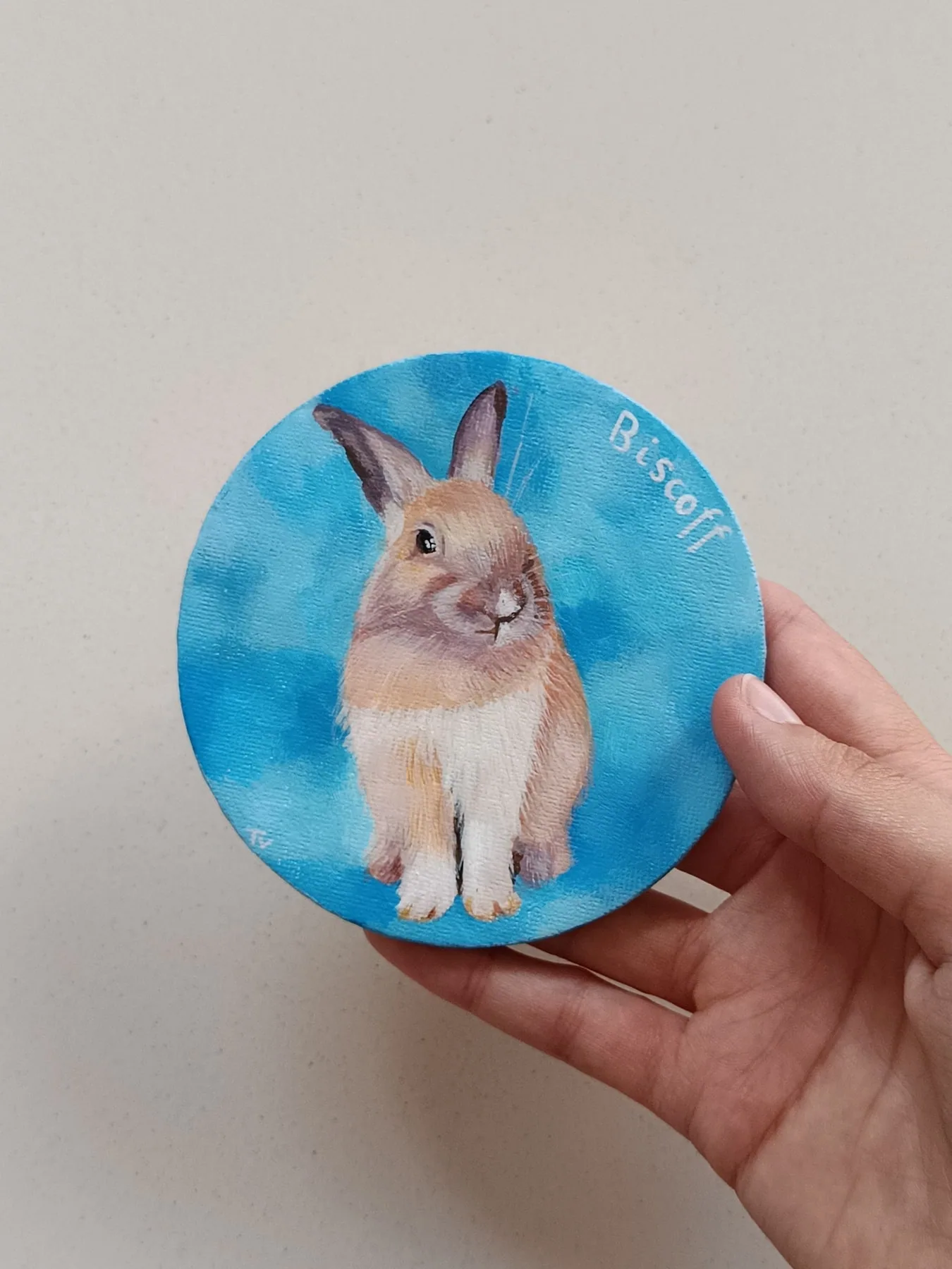Hand-painted rabbit fridge magnet on a round blue background, held in hand.