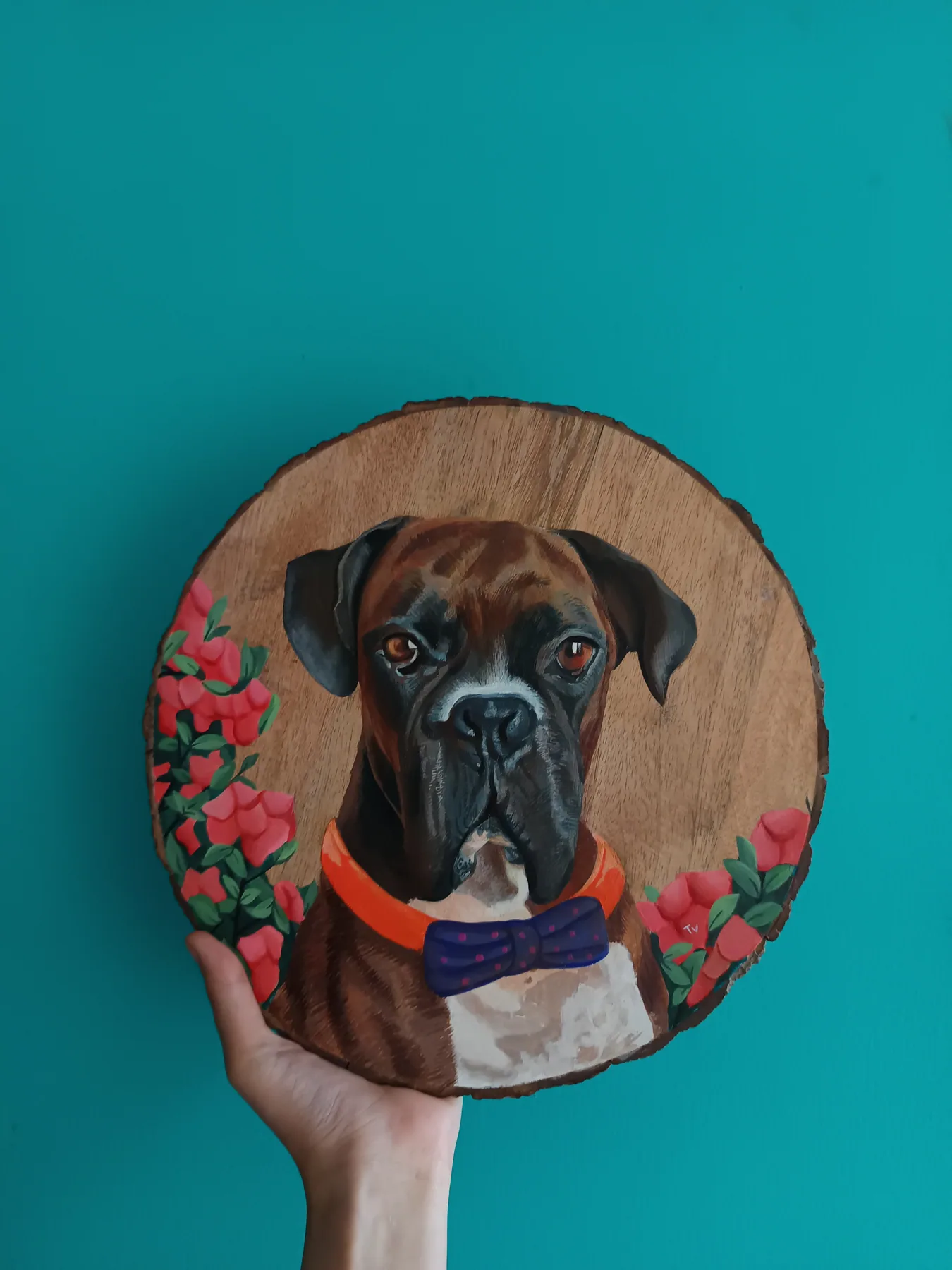 Round wood slice painting of a dark dog framed by red flowers, a bold custom pet portrait on natural wood.