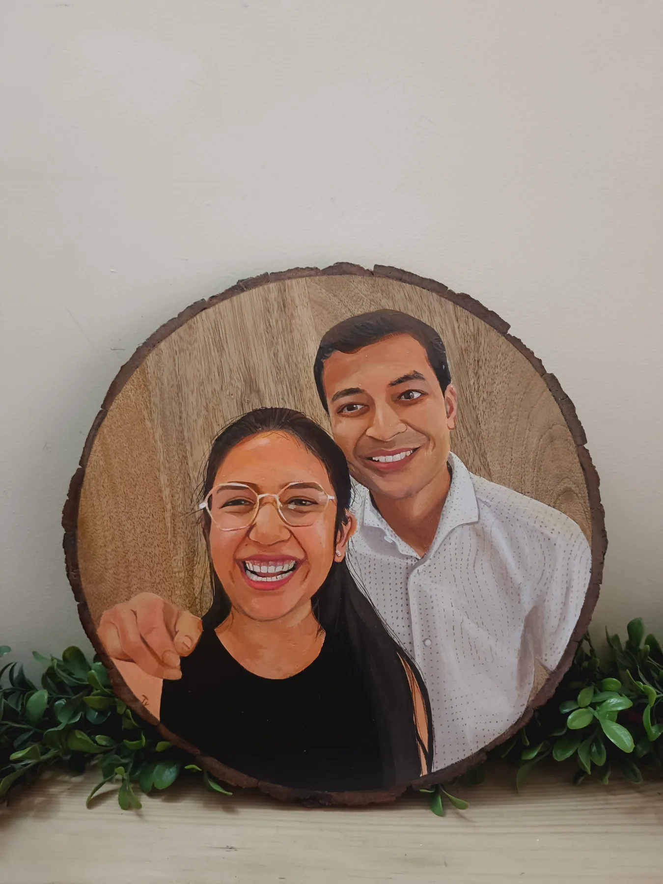 Round wood slice portrait of a smiling couple, displayed with greenery as a personalised handmade gift sample.