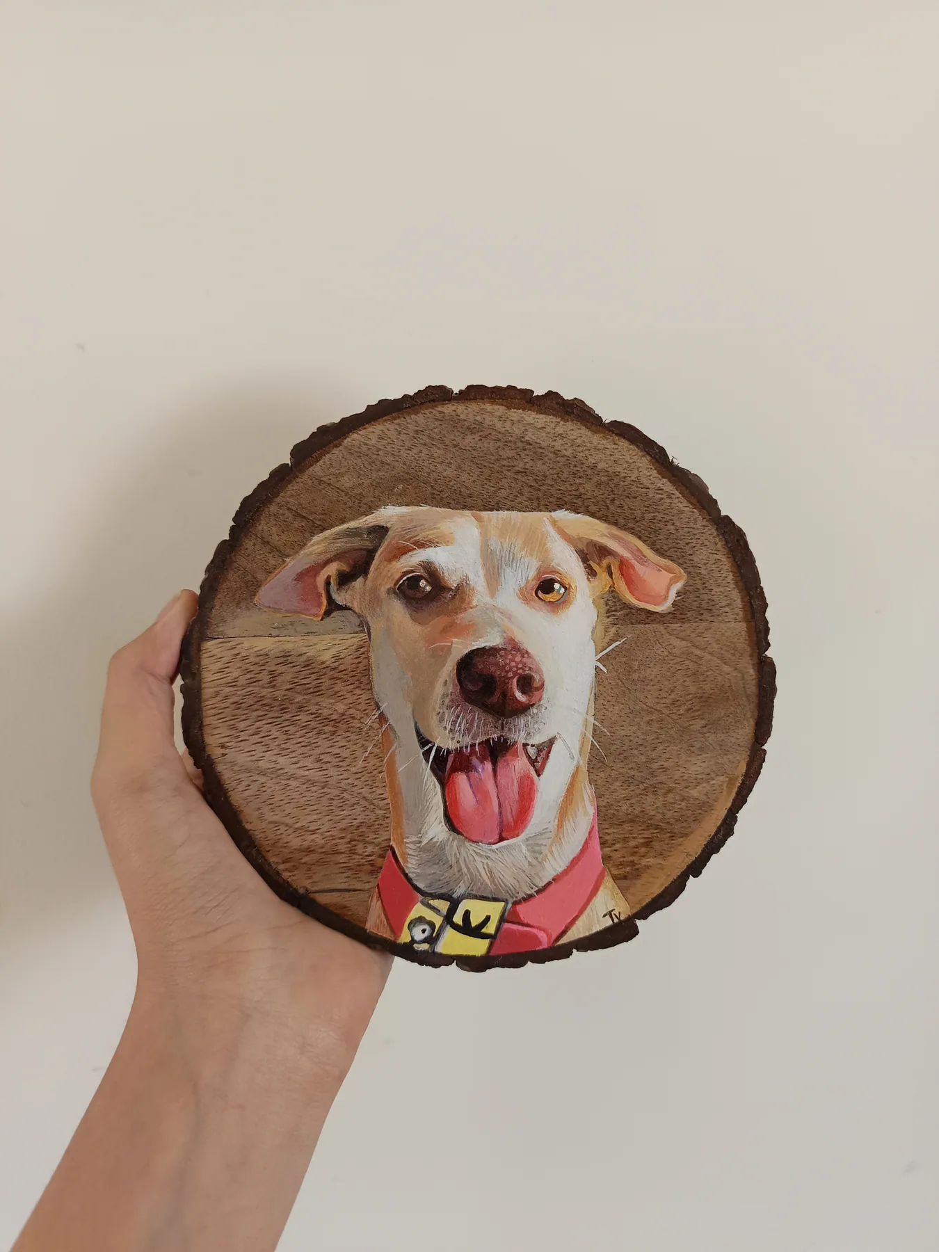 Small round wood slice painting of a smiling dog with a red collar, held up as a cheerful pet portrait sample.
