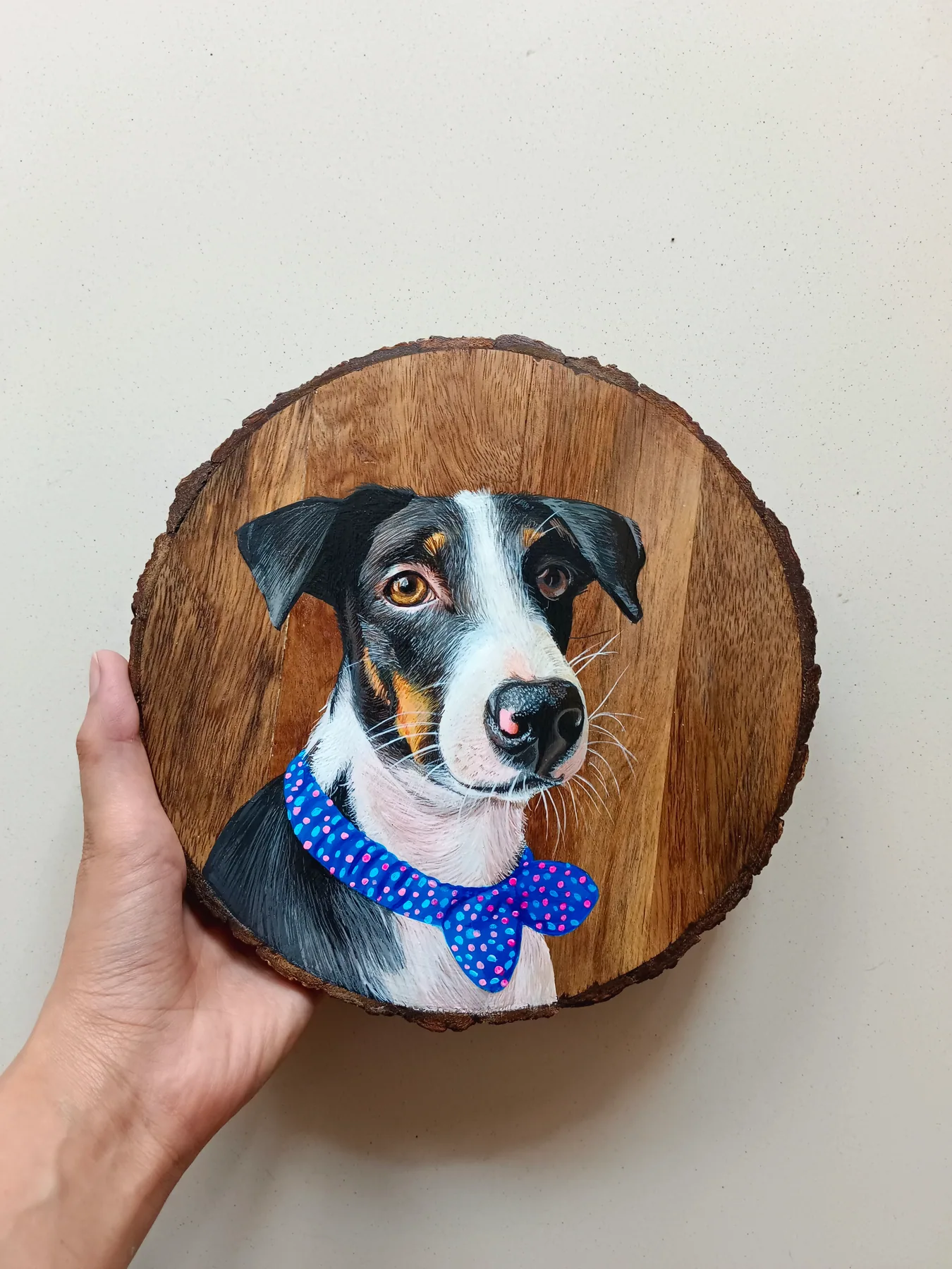 Small round wood slice painting of a black and white dog in a blue sweater, held in hand as a pet portrait.